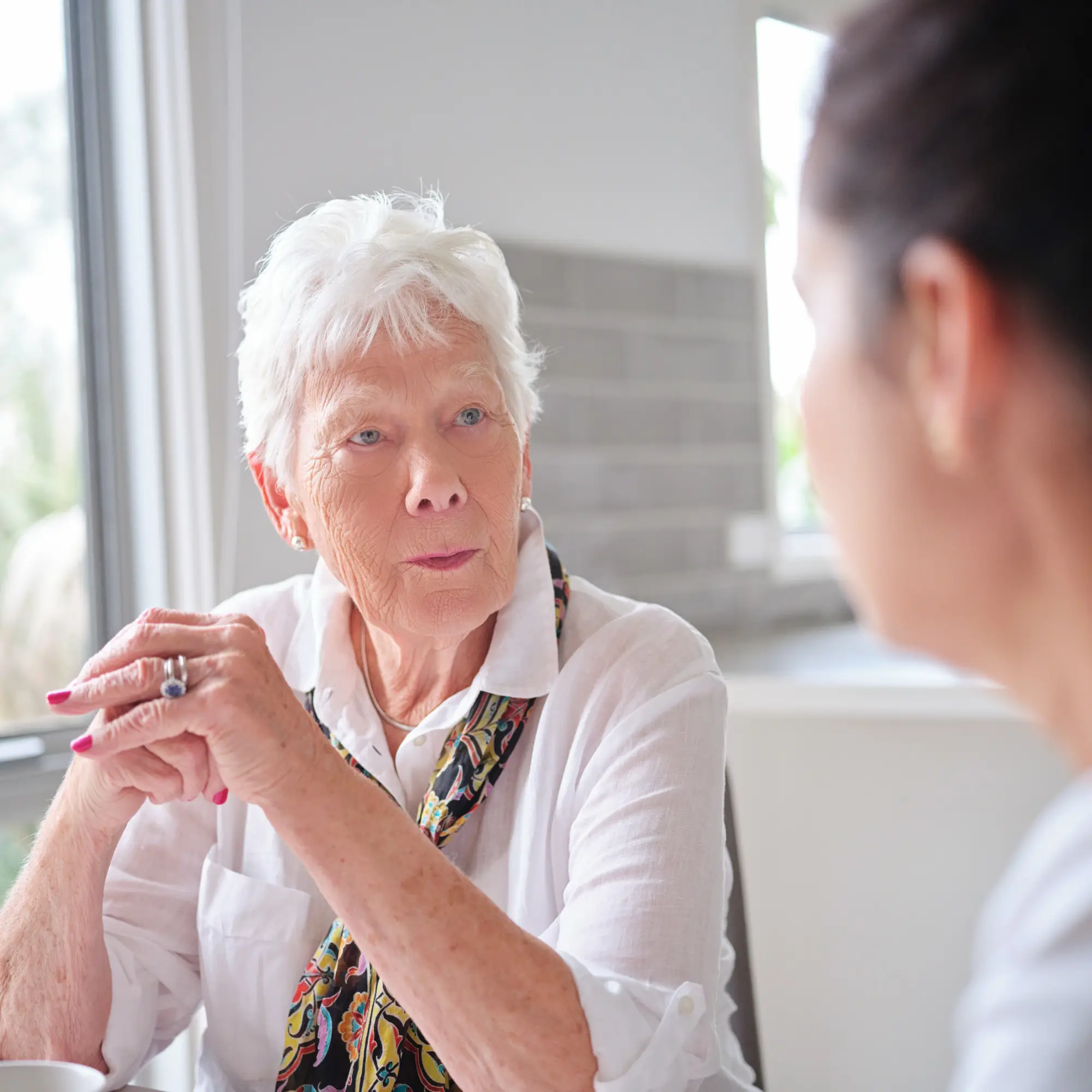 A carer sitting close and listening gently to an older woman at home.