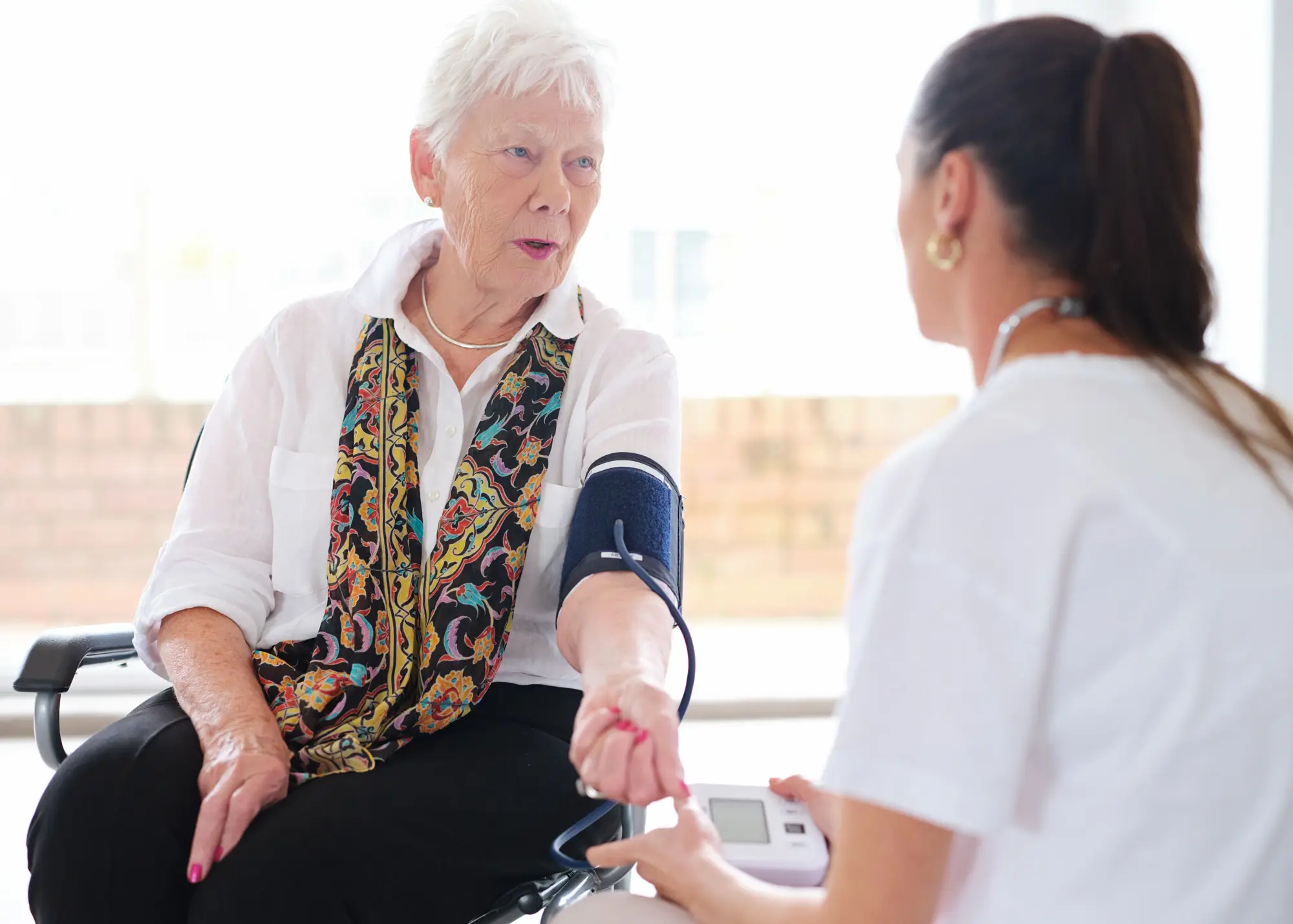 A nurse checking an older woman's blood pressure in her own living room.
